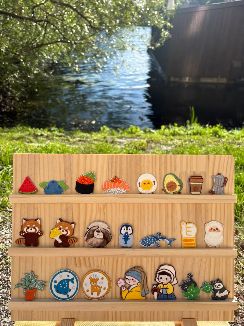 Rows of embroidered patches, from fruit to animals and characters, displayed on wooden shelves beside the water