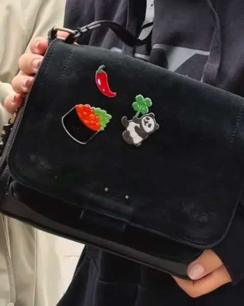 A chili pepper, sushi and four-leaf-clover panda patch on a black crossbody bag