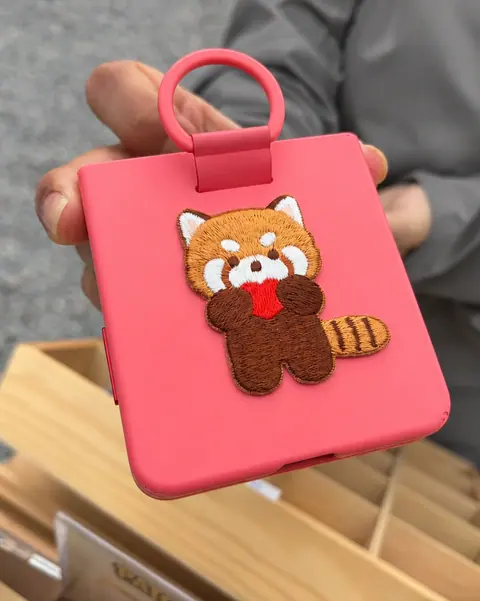 A red panda patch on a pink phone accessory with a ring grip