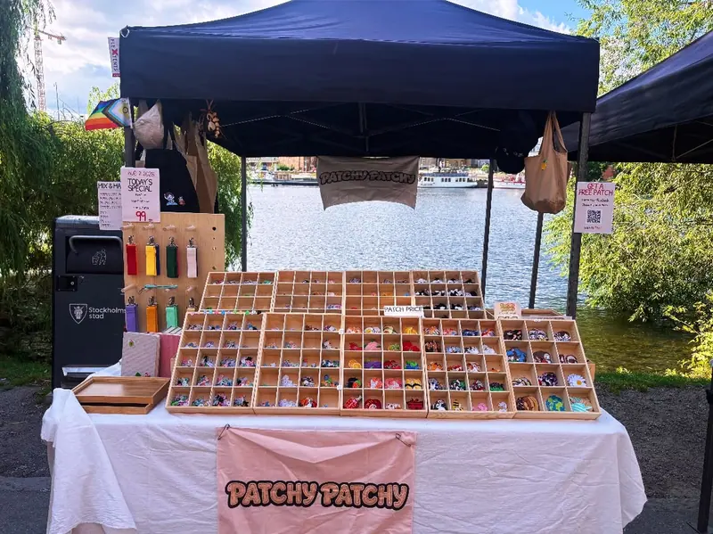 The Patchy Patchy market tent beside the water in Stockholm, with wooden trays of embroidered patches on a white table