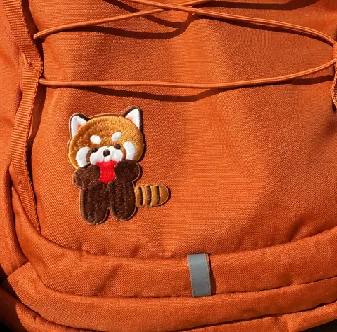A red panda patch sewn onto the front pocket of an orange backpack